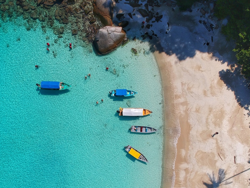 Vogelperspektive auf sonnigen Strand mit azurblauem Wasser und bunten Booten