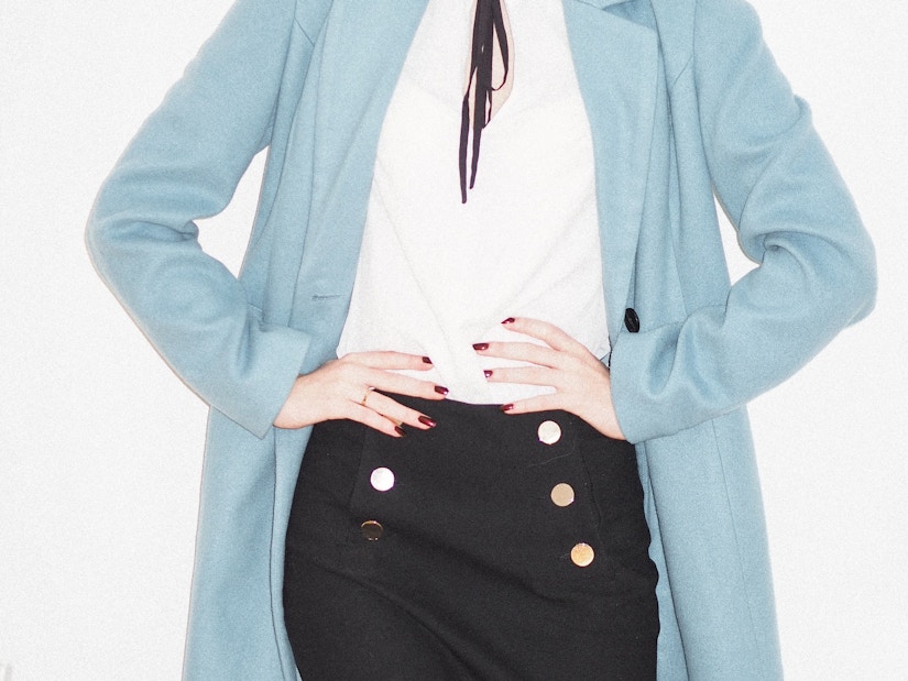 Frau trägt schwarzen Rock mit weißer Bluse und hellblauer Jacke