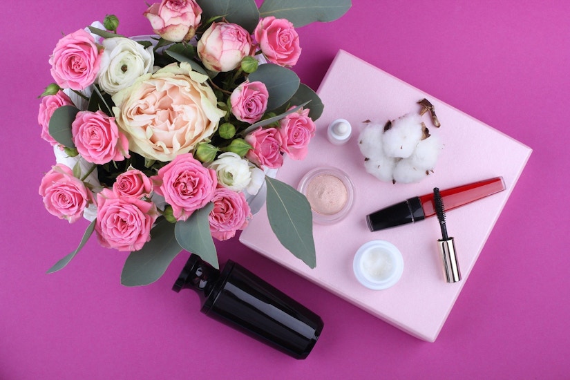 Kosmetik auf einem pinken Tisch mit Blumenstrauß.