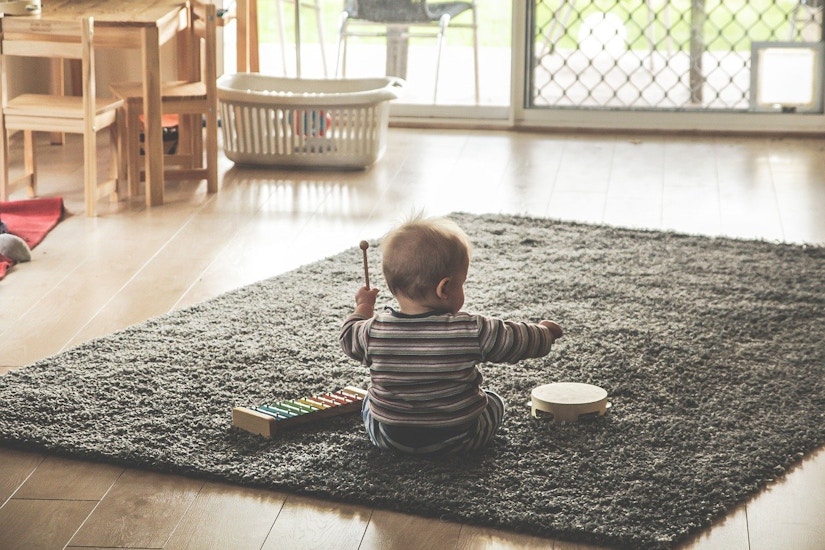 Baby sitzt auf flauschigem grauen Teppich und spielt einhändig Xylophon