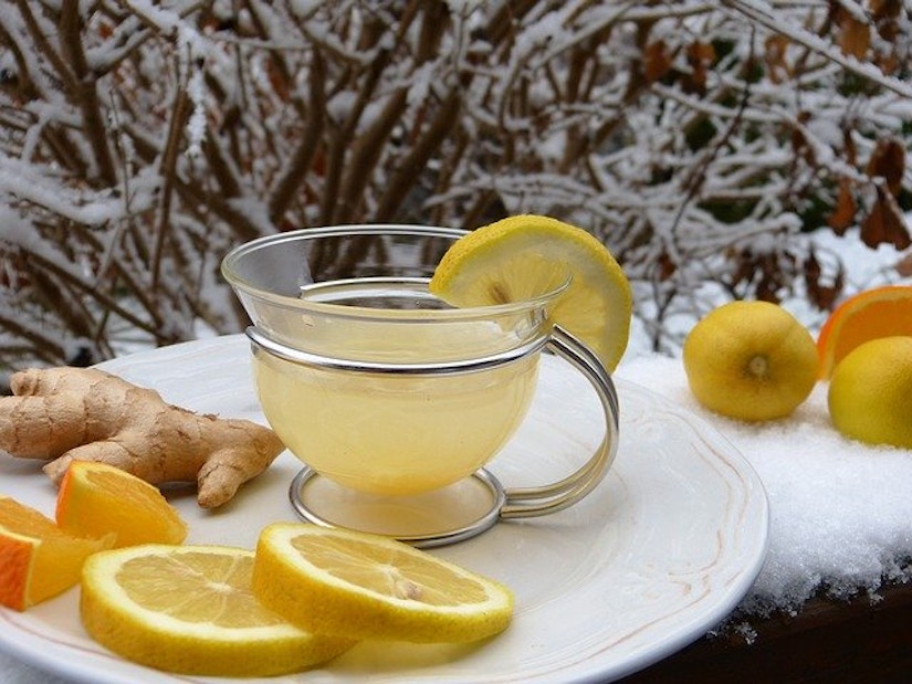 Tasse mit Ingwertee auf schneebedeckter Mauer. Umgeben von Zitronen und Ingwerstück.