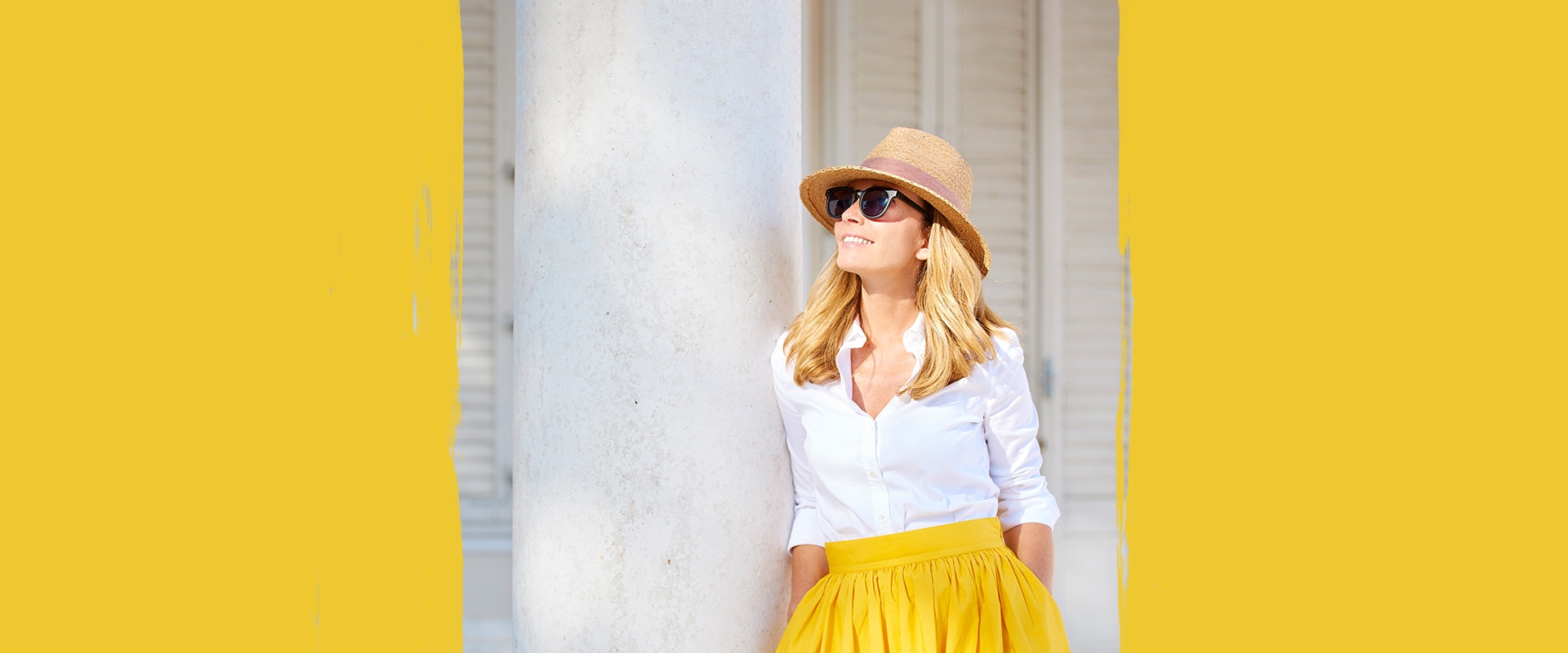 Eine Frau mit gelbem Rock, Hut und Sonnenbrille.