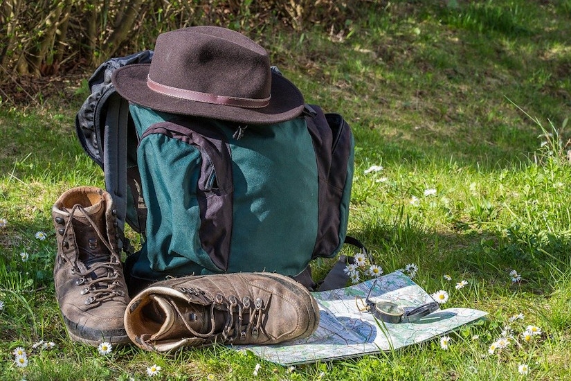 Rucksack, Hut, Karte und Kompass mit Wanderschuhen im Gras