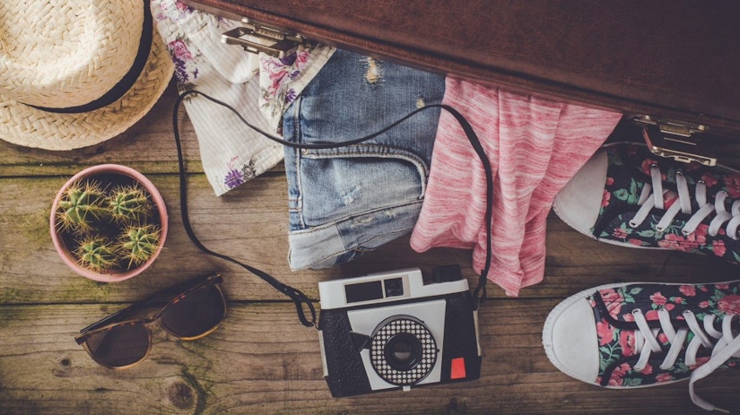 Ein Reisekoffer mit Kleidung, Schuhen, Kamera, Sonnebrille und Hut.