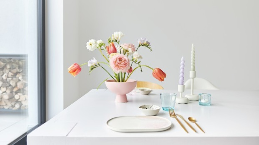 Ein Tisch mit einer Vase und Blumen, einem Teller, Besteck und Kerzenhaltern.