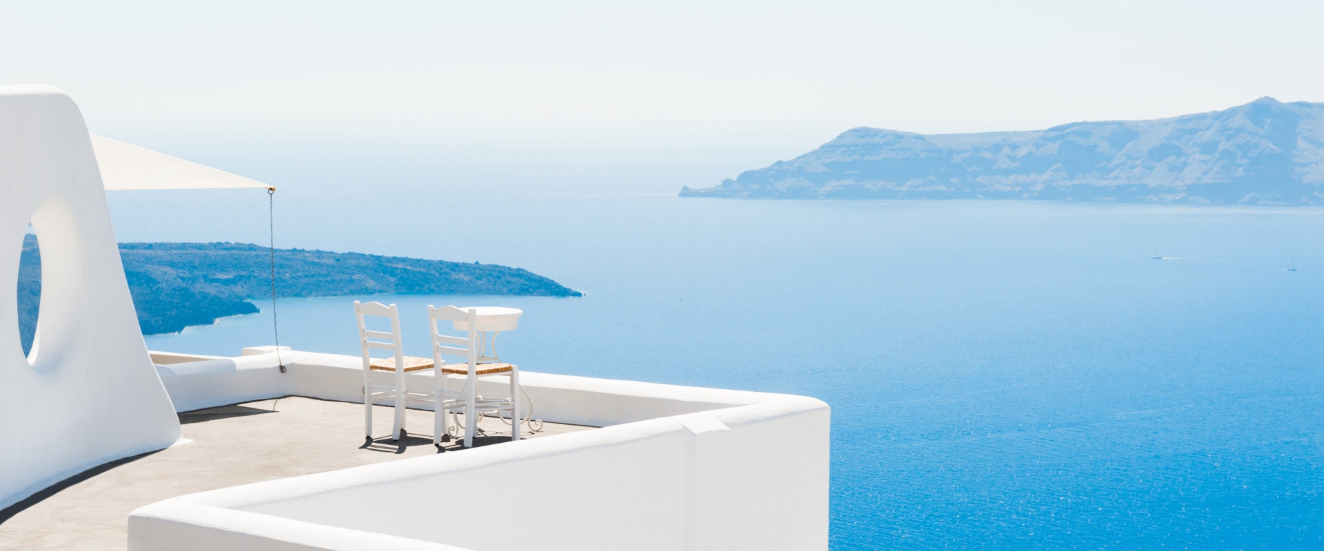 Zwei Stühle auf einer Terrasse. Im Hintergrund Meer.