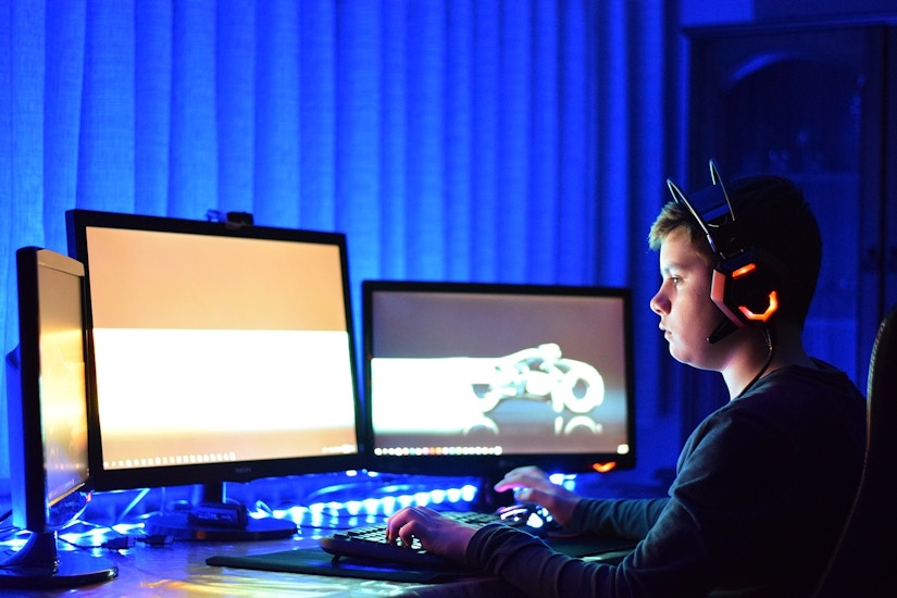 Jugendlicher Gamer sitzt im Dunkeln vorm PC Bildschirm