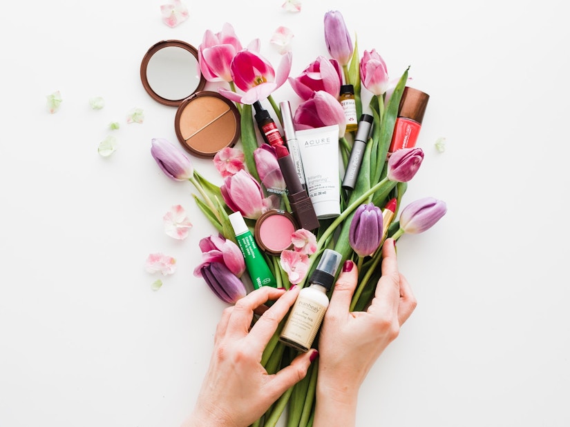 Frau, die Blumenstrauß und verschiedene Kosmetikprodukte in den Händen hält
