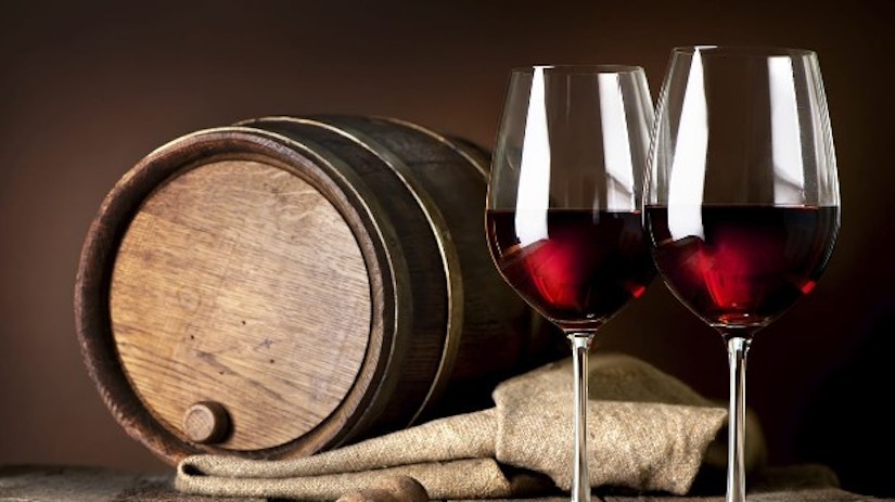 Zwei Weingläser mit Rotwein vor einem Weinfass.