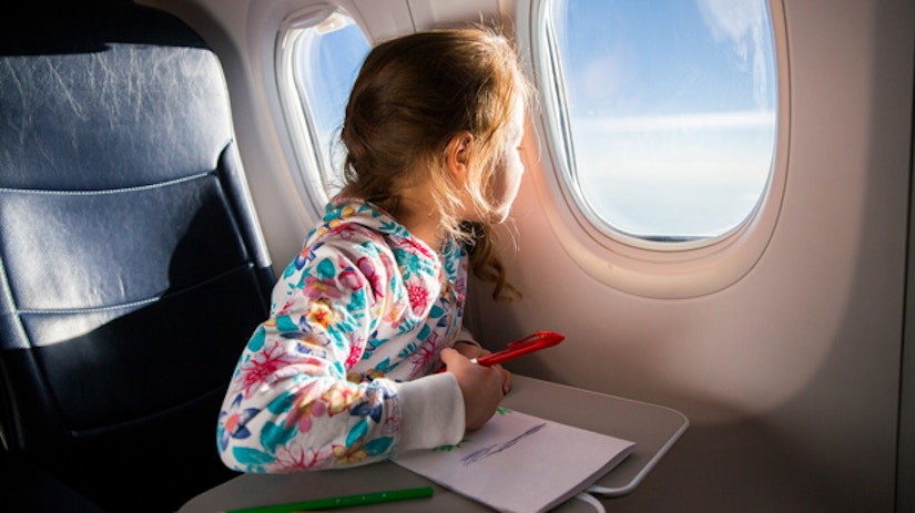 Ein Mädchen sitzt im Flugzeug und guckt aus dem Fenster.