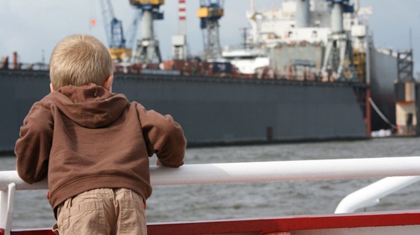 Ein Junge guckt am Hamburger Hafen auf ein Frachtschiff.