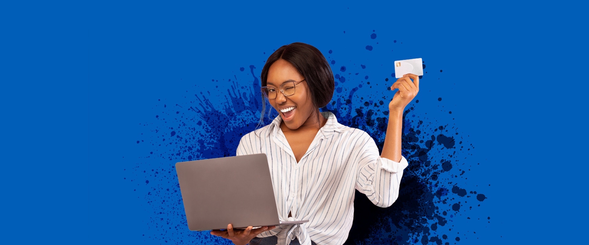 Eine junge Frau trägt einen Computer, hält eine Kreditkarte hoch und zwinkert.