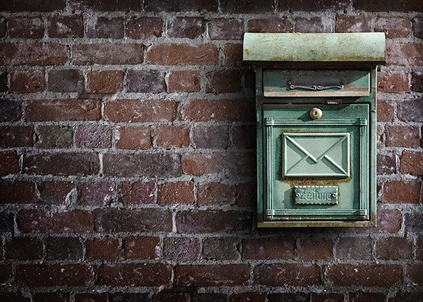 Ein grüner Briefkasten an einer Steinmauer