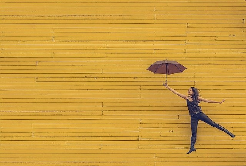 Frau mit Regenschirm vor gelber Wand