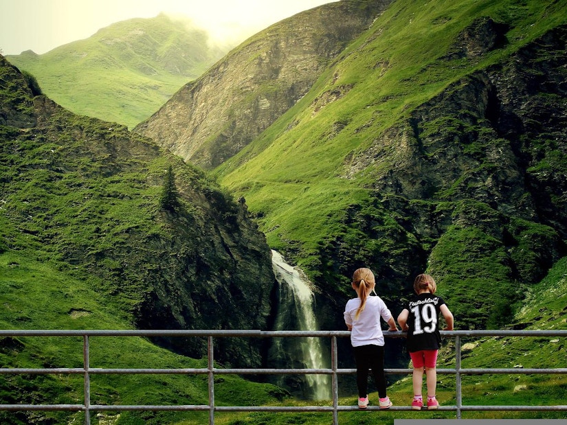 Kinder stehen auf dem Geländer vor dem Wasserfall in den Bergen