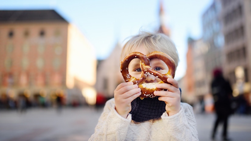 Ein Junge hält sich eine Brezel vors Gesicht.