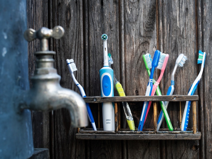 Bunte Zahnbürsten und eine elektrische Oral-B Zahnbürste neben einem urigen Wasserhahn.