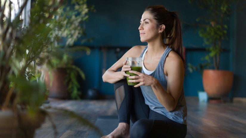 Eine Frau sitzt auf einer Yoga-Matte. Sie trinkt einen Smoothie.