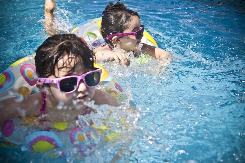 Zwei kleine Mädchen planschen mit ihren Schwimmreifen im Pool. 