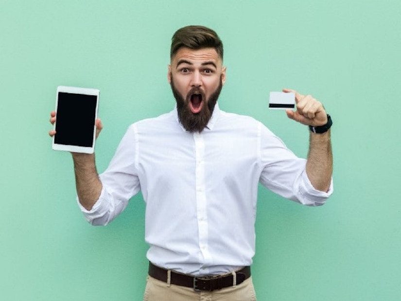 Ein Mann steht vor grünem Hintergrund und hält eine Kreditkarte sowie ein Tablet in der Hand.